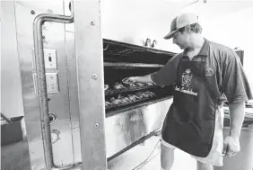  ?? STAFF PHOTOS BY DAN HENRY ?? Restaurant manager Andrew Hennen checks the temperatur­e of chicken in the smoker at the new location of Bones Smokehouse at 7601 E. Brainerd Road on Friday.