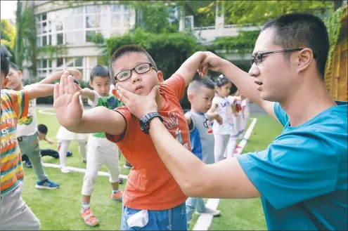  ?? JI CHUNPENG / XINHUA ?? Children at a kindergart­en in Nanjing, capital of Jiangsu province, practice kung fu with a teacher. Schools in China are looking to recruit more male teachers.