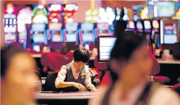  ??  ?? SOLITAIRE: Croupiers stand idle at card tables in the Sands Cotai Central casino resort, owned by billionair­e Sheldon Adelson’s casino operator Las Vegas Sands Corp.