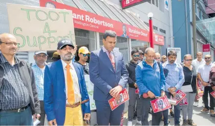  ?? Photo /Mark Mitchell ?? Wellington Indian Associatio­n president Dipak Bhana , centre, with dairy owners holding a minute’s silence outside Grant Robertson’s electorate office in Wellington.