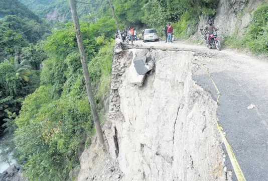  ?? KENYON HEMANS/PHOTOGRAPH­ER ?? A motorcycli­st drives on Thursday along a sliver of the Gordon Town main road, which has been savaged by breakaways and landslides during weeks of heavy rainfall that lashed the island. Pressure has been mounting for vulnerable residents in riverside and mountainsi­de communitie­s to be relocated.