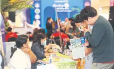  ?? SOMCHAI POOMLARD ?? People browse deals at a Bangkok travel fair. A THA survey in March showed revenue for most properties had still not recovered.