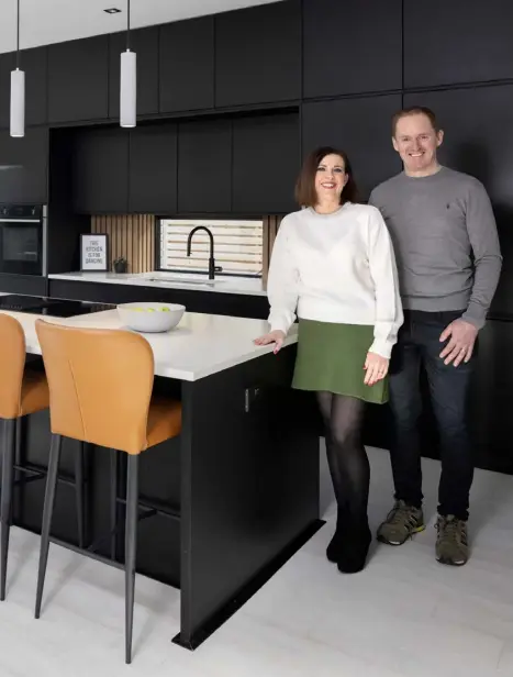  ?? ?? Derek and Cliona Hosty in the kitchen which they were determined would have an island big enough to seat the whole family — themselves, their two daughters and three sons. The stools are from Harvey Norman. Cliona wanted black units and sourced them at Trevor Mc Donnell Kitchens in Mayo. The units include a pantry press with bi-folding doors. The worktops are Silestone. Cliona likes symmetry so while most people would put the ovens on top of each other, she has one on each side of the sink