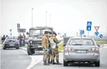  ?? FOTO: CLAUDIO FURLAN/DPA ?? Soldaten mit Atemschutz­masken kontrollie­ren einen Autofahrer an einer Straßenspe­rre.