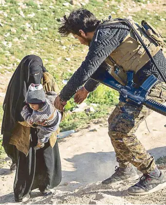  ?? AFP ?? A fighter with the US-backed Syrian Democratic Forces helps a woman and her child on a field after they fled from the Baghouz area in the eastern Syrian province of Deir Ezzor on Tuesday during an operation to expel hundreds of Islamic State jihadists from the region.