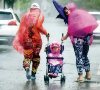  ??  ?? September 17, 2018: Near the Wanbo Center in Guangzhou, a couple of parents fasten their child in a buggy and drag it in the heavy rain and wind. Mangkhut brought continuous precipitat­ion to Guangdong Province. VCG
