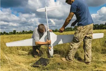  ?? DAVID GUTTENFELD­ER/THE NEW YORK TIMES ?? Ukrainian troops practice attaching a dummy bomb to the undercarri­age of a Punisher, a high-end fixed-wing military drone manufactur­ed in Ukraine, on July 25 in an open field on the outskirts of Kyiv.