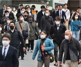  ?? — AFP photo ?? Commuters walk on a street in Shinjuku district of Tokyo on March 13 on the first day of reduced mask requiremen­ts.