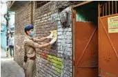  ?? — PTI ?? A policeman pastes a notice at the residence of a Covid-19 positive muezzin (who recites prayer-call at mosques) in Dehradun on Tuesday.