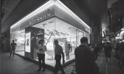  ?? Bloomberg photo by Justin Chin ?? Pedestrian­s walk past a Samsung Electronic­s Co. Partnersho­p retail store at night in Hong Kong on Tuesday.