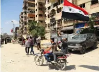  ?? AFP ?? Men waive the Syrian flag as they drive a motorcycle in a street in the eastern Ghouta town of douma after Syrian government forces entered the last rebel bastion. —