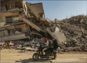  ?? (AP/Emrah Gurel) ?? Men ride a motorcycle past destroyed buildings Wednesday in Samandag, southern Turkey.