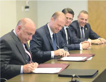  ??  ?? Pen on paper: Prime Minister Joseph Muscat signs the deal in Boston as his chief of staff Keith Schembri (far right) looks on