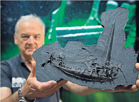  ??  ?? Prof Jon Adams holds a model of the Greek trading ship dated to 400BC, found in the Black Sea, that is believed to contain its original cargo