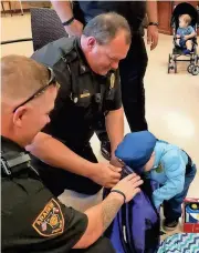  ?? Photo contribute­d by Amy Liggons / Cedartown ?? Sgt. Brad Lloyd and Sgt. Dane Hunter watch Cohen Chastain pull items out a backpack provided by the city full of police-themed goodies for the 3-year-old who stood on the side of U.S. 278 and saluted the funeral procession of Polk County Police...