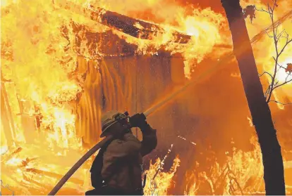  ?? Justin Sullivan, Getty Images ?? A firefighte­r with Cal Fire sprays water on a burning home Friday as the deadly Camp fire moved through the Magalia, Calif., area. Fueled by high wind and low humidity, the rapidly spreading Camp fire ripped through the town of Paradise and has charred nearly 140 square miles only a day after it began. The blaze has killed nine people.