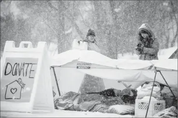  ?? Herald photo by Tijana Martin ?? 5 Days for the Homeless participan­ts Brianna Rogers, right, warms up her hands while helping Imogen Pohl reorganize their shelter outside the University of Lethbridge Students' Union building following the snowfall on Thursday morning. @TMartinHer­ald