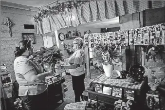  ?? [JOHN MINCHILLO/ASSOCIATED PRESS PHOTOS] ?? Susan Hern, right, who runs a craft store in Corning, Ohio, hands a poinsettia to Malana Monson, a local bakery owner.