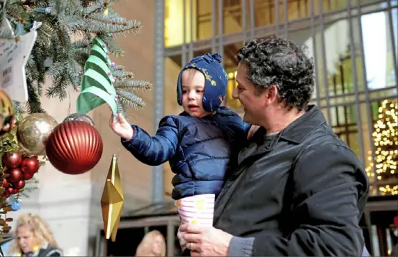  ?? Clare Sheedy/Post-Gazette ?? Isaak Mogush, 2, and his father, Rudy Mogush, look at the ornaments on the tree outside the City-County Building, Downtown, on Saturday before the 106th City of Pittsburgh Tree Lighting and Zambelli Rooftop Fireworks show at Light Up Night.