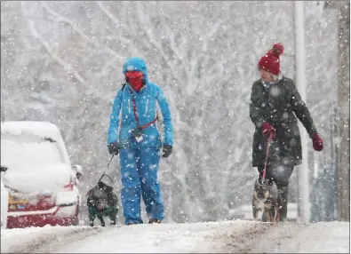  ?? ?? Women walk their dogs in the snow-covered streets of Tomintoul, while George Popescu and one-year-old daughter Arya were sledging in Cairngorms National Park