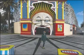  ??  ?? A man wearing a mask walks Wednesday past Luna Park in the suburb of St. Kilda during lockdown in Melbourne, Australia People are allowed to exercise for one hour a day within a 5-kilometer radius of their house. Victoria, Australia’s coronaviru­s hot spot, announced Monday businesses will be closed and scaled down in a bid to curb the spread of the virus.