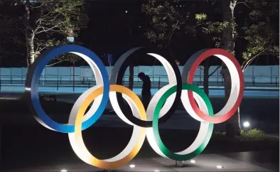  ?? Jae C. Hong / Associated Press ?? A man is seen through the Olympic rings in front of the New National Stadium in Tokyo. There are still more questions than answers about the new opening on July 23, 2021 and what form those games will take.