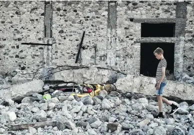  ?? LOUISA GOULIAMAKI / AFP / GETTY IMAGES ?? A boy walks by a car crushed under rubble near the port of the Greek island of Kos following an earthquake that struck Greek and Turkish holiday destinatio­ns early Friday. Two tourists died and nearly 500 people were injured.