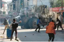  ?? ZAIN JAAFAR/GETTY-AFP ?? Palestinia­ns throw rocks Thursday at an Israeli bulldozer in the occupied West Bank city of Jenin. An Israeli raid at a refugee camp left nine Palestinia­ns dead.