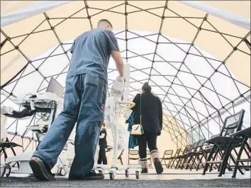  ?? Hayne Palmour IV San Diego Union-Tribune ?? EMERGENCY technician Kyle Heaston wheels equipment into a tent at Palomar Medical Center Escondido on Jan. 3. A surge in f lu cases has also forced hospitals to send away ambulances and cancel surgeries.