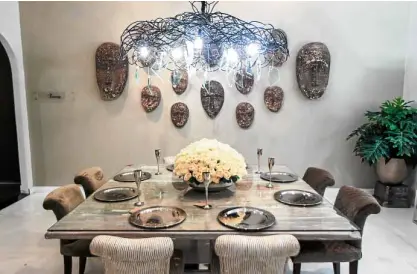  ??  ?? Tribal masks as wall details, a modern metal-and-glass chandelier, a dining table of wood in an old white finish, and off-white upholstere­d chairs make up the Eternity Room.