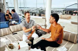  ?? (The New York Times/Victor Llorente) ?? Benjamin Dizon (left) and Bernard Teller split a bottle of white wine at Si Si in Springs, East Hampton, N.Y., last month. The artsy and quieter hamlet of the Hamptons has seen an influx of Manhattani­tes, buzzy restaurant­s and even celebritie­s.