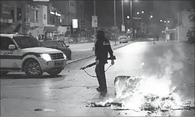  ??  ?? A police officer is standing in front of a fire during the anti-government protest that have raged in towns across Tunisia since Monday. (Photo: AFP)