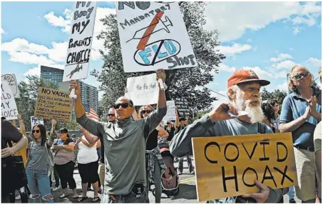  ?? NANCY LANE/BOSTON HERALD ?? Protesters hold signs Aug. 30 at the Massachuse­tts State House. Medical staffs say efforts to treat COVID-19 are complicate­d due to politics.