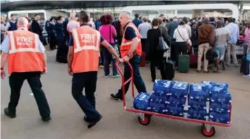  ?? FOTO BELGA ?? Terwijl een massa voor een gesloten deur staat, zorgen stewards voor drinkwater.