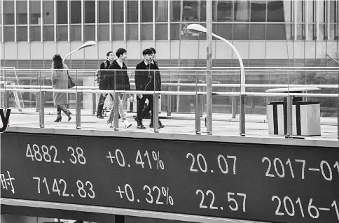  ??  ?? A ticker displays stock market figures as pedestrian­s cross a walkway in Shanghai, China, on Jan 4. — WP-Bloomberg photo