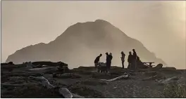  ?? PHOTO BY TOBIN HAHN ?? Gunderson Rock stands sentinel over a group of locals gathered at Greenwood Beach on a recent evening.