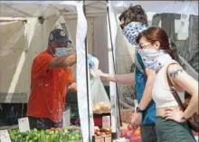  ?? Emily Matthews/Post-Gazette ?? Victor Torres, left, an employee with Simmons Farm, gives a bag of potatoes to Adam Wechter and Lauren Schrecker, both of the South Side, on May 24 at the 11th Street Farmers Market in the Strip District. It was the temporary name and location for the Market Square Farmers Market.