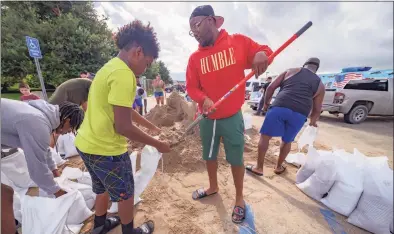  ?? Matthew Hinton / Associated Press ?? Jawan Williams shovels sand for a sandbag held by his son Jayden Williams, before landfall of Hurricane Ida in Chalmette, La., near New Orleans on Saturday. Hurricane Ida looks an awful lot like Hurricane Katrina, bearing down on the same part of Louisiana on the same calendar date. But hurricane experts say there are difference­s in the two storms 16 years apart that may prove key and may make Ida nastier in some ways but less dangerous in others.