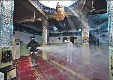  ?? Photograph­s by Haidar Hamdani AFP/Getty Images ?? HOUSES of faith have become a front line in the battle by government­s to smother the spread of the deadly coronaviru­s. Above, a mosque where a case of the virus was recently confirmed gets disinfecte­d in Najaf, Iraq.