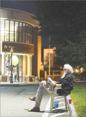  ?? H John Voorhees III / Hearst Connecticu­t Media ?? Chris Maloney, of Danbury, reads a mystery novel under a street light as he and other homeless people prepare to spend another night last week sleeping in tents in front of Danbury City Hall to protest the closing of the Jericho Partnershi­p shelter.