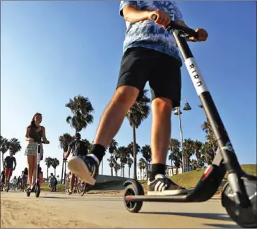  ?? MARIO TAMA/GETTY IMAGES NORTH AMERIC/AFP ?? People ride electric scooters along Venice Beach in Los Angeles, California. Some city residents complain the e-scooters are dangerous for pedestrian­s and clog sidewalks.