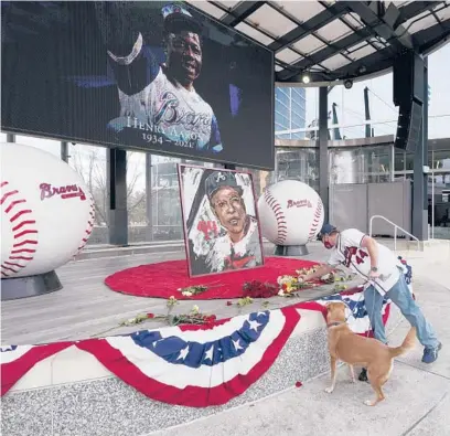  ?? JOHN BAZEMORE/AP ?? A man places flowers next to a portrait of Braves’ Hank Aaron on Friday outside Truist Park in Atlanta.