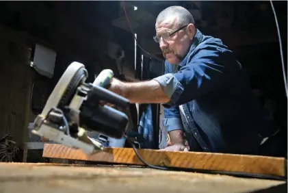  ?? STAFF PHOTOS BY TROY STOLT ?? Cotton Gin Antiques store owner Danny Brown uses a saw to cut a piece of repurposed wood for a table on Tuesday in Ringgold.