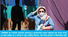  ?? — AFP ?? TEHRAN: An Iranian woman wearing a protective mask adjusts her head scarf as she walks on a street in the capital Tehran. The holy month of Ramadan will begin today in Iran, the office of the Islamic republic’s supreme leader announced yesterday.