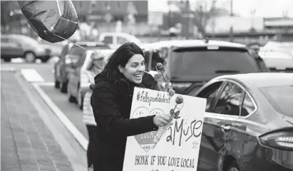  ?? BARBARA HADDOCK TAYLOR/BALTIMORE SUN ?? Claudia Towles, owner of Amuse Toys in Fells Point, passes out flowers to drivers to welcome them downtown Wednesday.