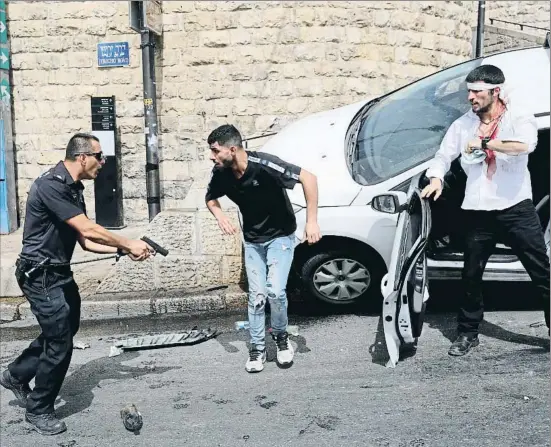  ??  ?? Un policia israelià davant d’un palestí i un jueu ferit al ser atacat el seu cotxe per joves palestins al carrer Jericó de Jerusalem