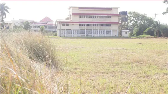  ?? (Photo by Keno George) ?? A view of the weeded section of the Queen’s College field as seen yesterday, bordered by overgrown grass, which is kneehigh in some places. The east wing of the school is visible in the background.