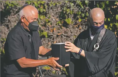  ?? (AP/Jae C. Hong) ?? C lyde Matsumuram (left) hands a small box containing the ashes of his grandfathe­r, Giichi Matsumura, to Shumyo Kojima, a head priest of Zenshuji Buddhist Temple, during a memorial service at Woodlawn Cemetery in Santa Monica, Calif.