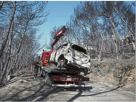  ?? — AP ?? Nothing to salvage: A worker transporti­ng a burnt car following a wildfire in Neos Voutzas, east of Athens.