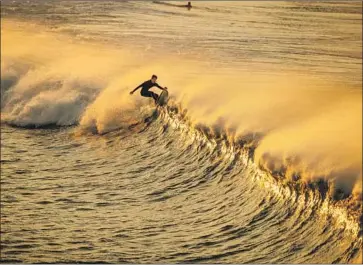  ?? Photograph­s by Allen J. Schaben Los Angeles Times ?? A GOLDEN SUNRISE illuminate­s a Santa Ana winds-swept wave for a surfer at the Huntington Beach Pier. Up the coast, gusts hit 67 mph in the Malibu Hills, said a National Weather Service meteorolog­ist in Oxnard.